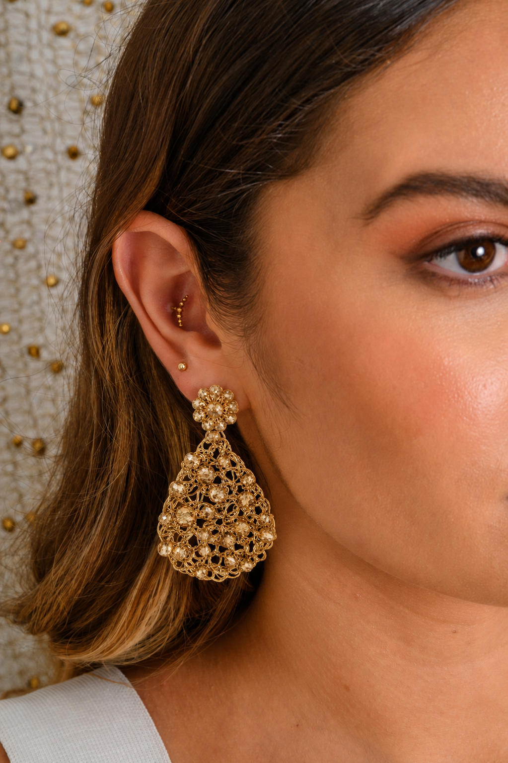 Close-up of a woman wearing gold earrings with a neutral background. Handmade in Brazil, these teardrop mesh earrings feature 18 karat gold filled wire, multicolor crystals, lightweight comfort, and hypoallergenic materials.