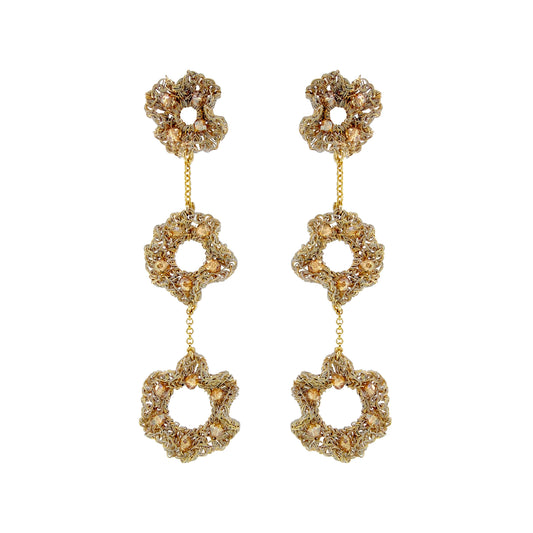 A pair of gold-tone dangle earrings with three stacked flower-shaped links, each adorned with clear rhinestones and accented with small gold beads, set against a plain white background. Hand-crocheted gold ruffled cascade earrings with three floral drops and champagne crystal accents, handmade in Brazil.