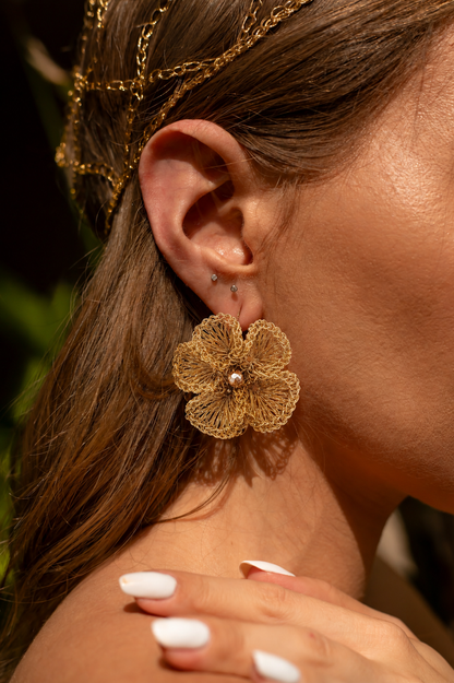 Close-up of a woman wearing gold floral earrings and a headpiece.