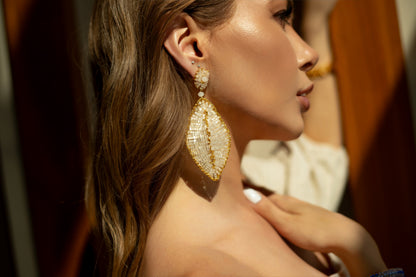 Close-up of a woman wearing gold earrings with a blurred background. hand-crocheted earrings, 18k gold-filled earrings, leaf earrings, handmade Brazilian jewelry, lightweight statement earrings, hypoallergenic earrings.