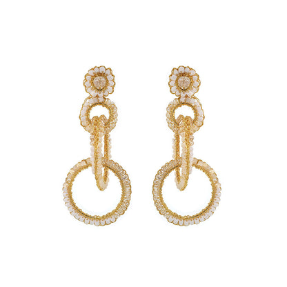 A pair of gold-filled, hand-crocheted earrings with sparkling crystals, featuring interlocked links and floral details. Interlocked link hand-crocheted earrings handmade in Brazil with 18 karat gold filled wire, soft ivory beads, sparkling crystal accents, and layered circular links.